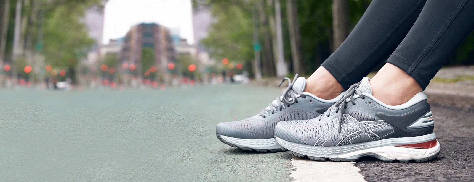 Closeup of gray running shoes on a woman sitting outside on a curb.
