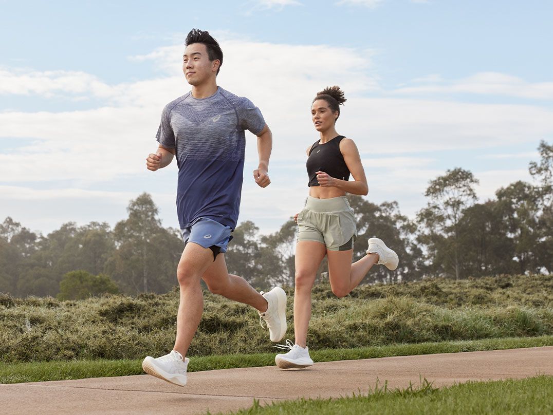 Male and female runner run on a cement path out in a park