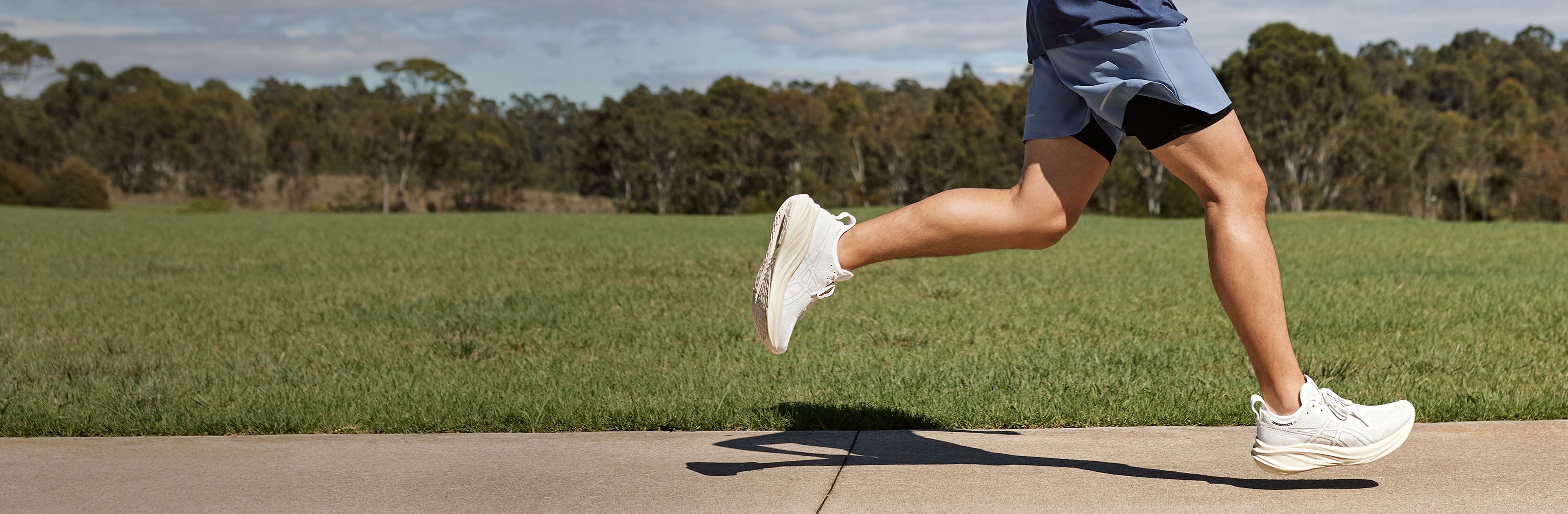A male runner runs outside in the new Gel-Nimbus™ 26 shoe. You can only see him from the waist down.