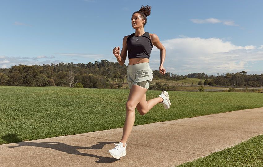 A female runner runs in a black crop top and pale green shorts wearing the new Gel-Nimbus™ 26 shoes.