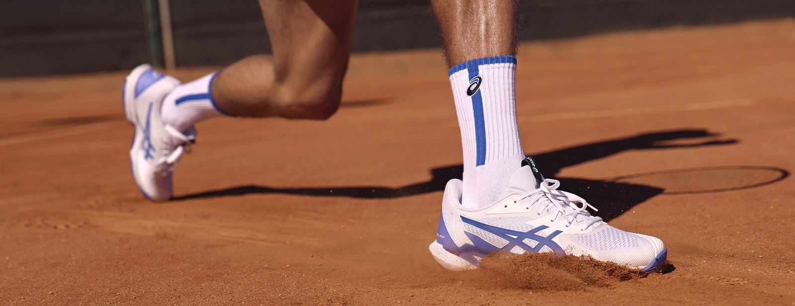 Close up of Alex de Minaur wearing the new SOLUTION SPEED™ FF 3 shoe, pictured from the knee down on a red clay court.