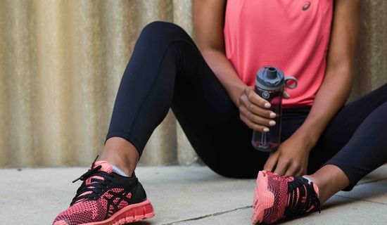 woman in pink top with pink & black running shoes & holding a waterbottle; shoes are the main focus