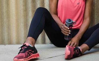woman in pink top with pink & black running shoes & holding a waterbottle; shoes are the main focus