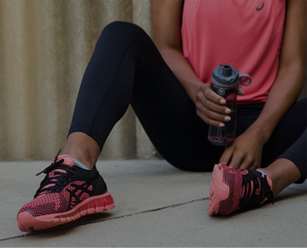 Woman in pink shoes, pink top and black leggings sitting and holding a water bottle.
