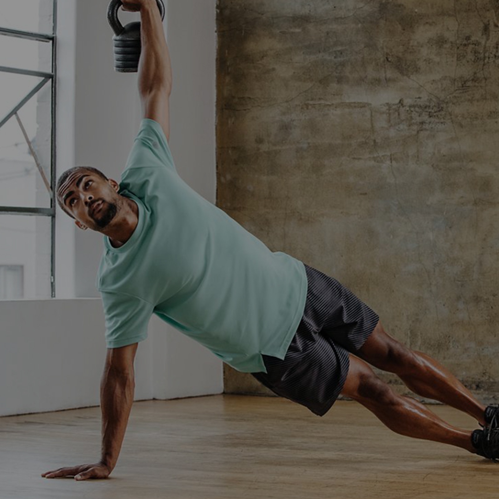 Man in a turquoise shirt and gray shorts doing a side plank.