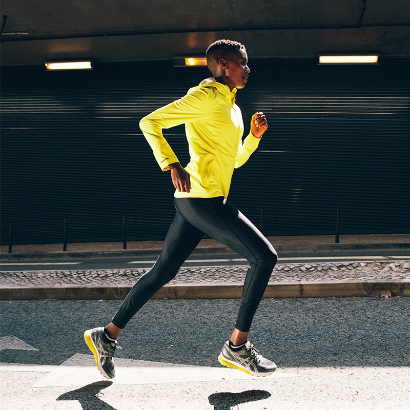 Woman running down street wearing yellow and grey nimbus 21 running shoes