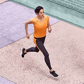 Woman running in GEL-CUMULUS 23 (high angle, orange and black activewear)