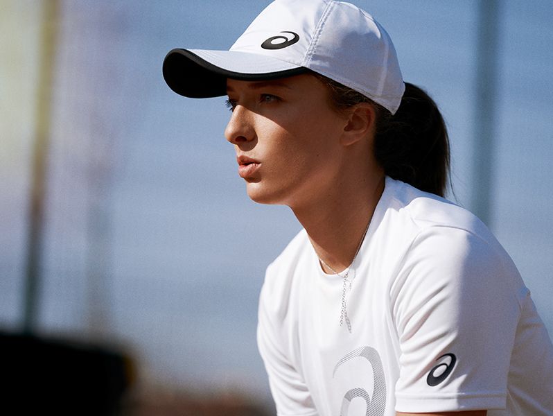 Female tennis player in white ASICS hat and white ASICS tshirt.