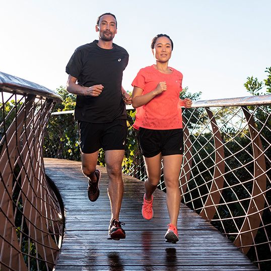 Make and female runners jogging across wooden bridge.