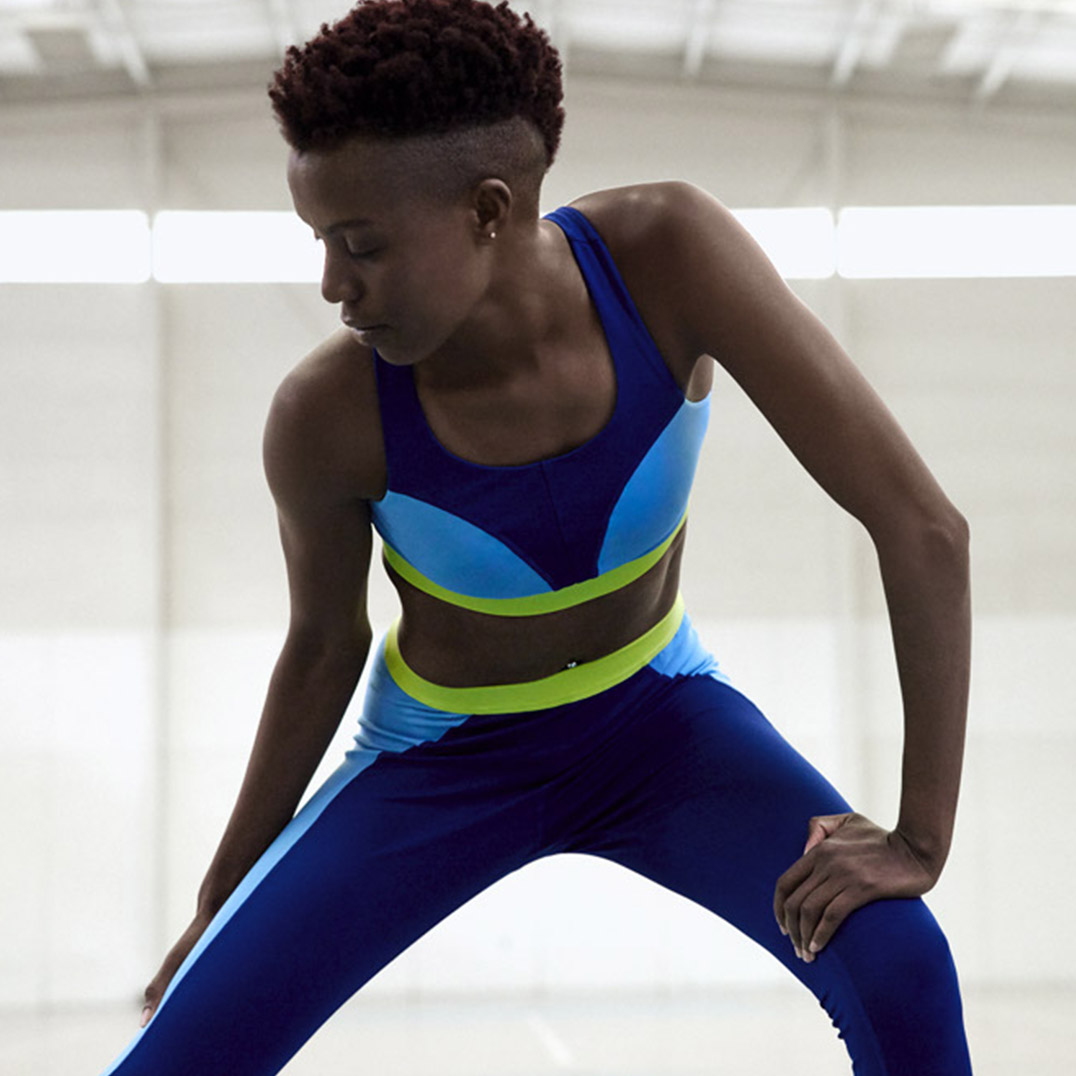 Diane Nukuri stretching inside a while gymnasium. She is wearing a matching ASICS set. 