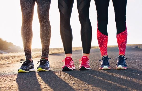 Closeup of three pairs of legs wearing leggings and running shoes at sunset.