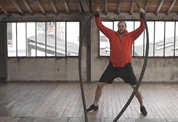 Man doing jumping jacks while holding ropes.