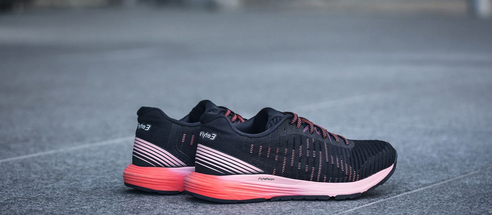 Women’s black and pink running shoes sitting on pavement.