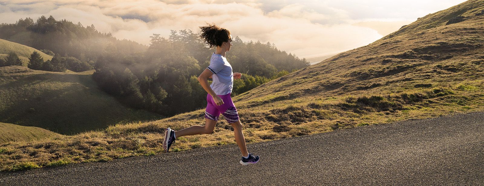 Woman running on mountain in ASICS clothing.