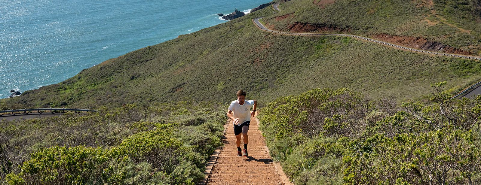 Man running up stairs near coastline in ASICS clothing.