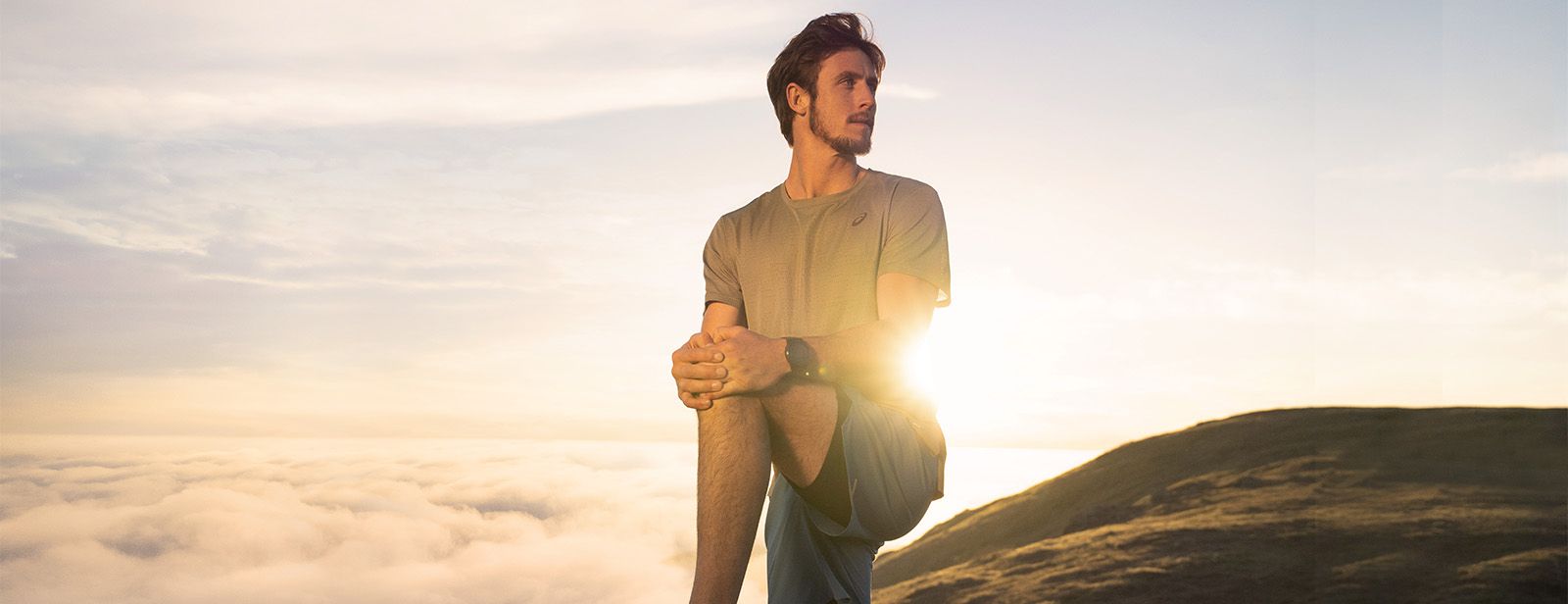 Man stretching on mountain top with ASICS clothing.