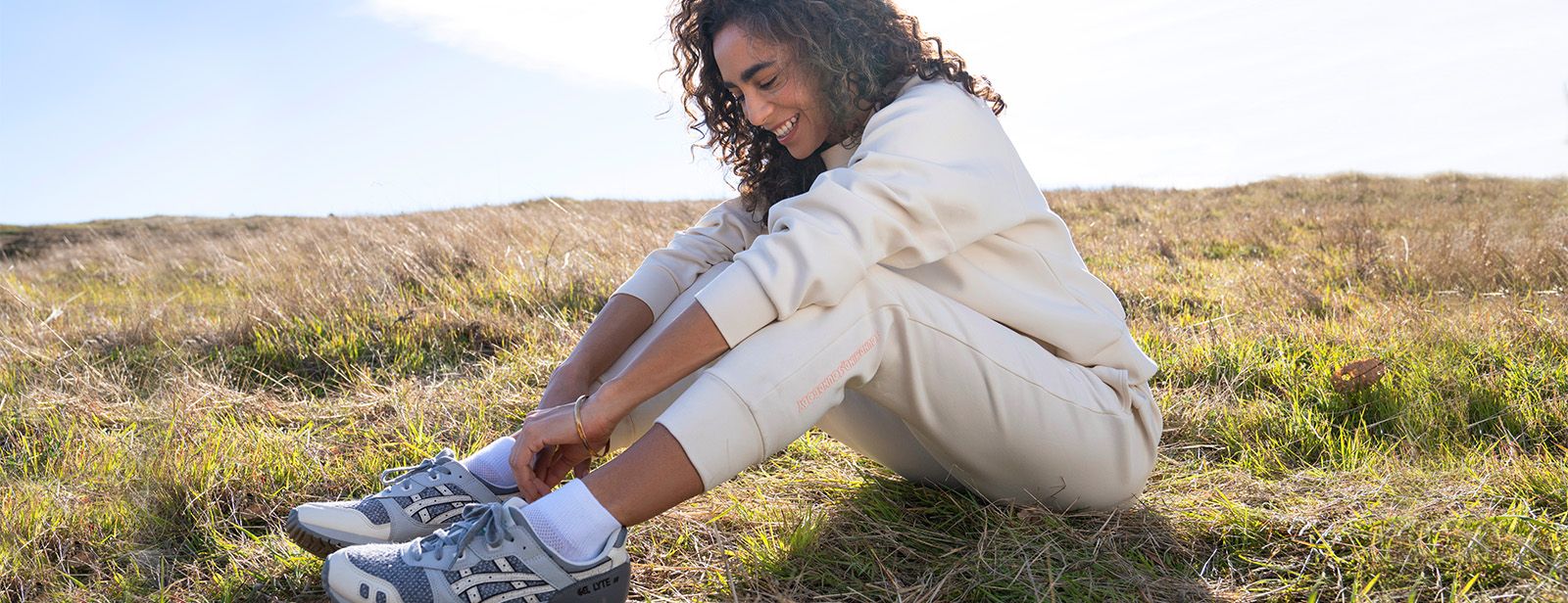 Woman sitting in field in ASICS clothing.