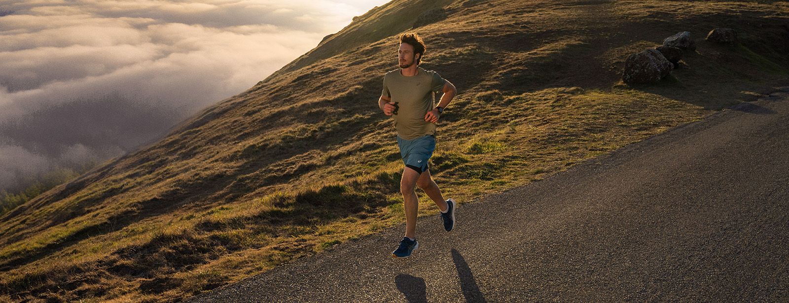 Man running on mountain top with ASICS clothing.
