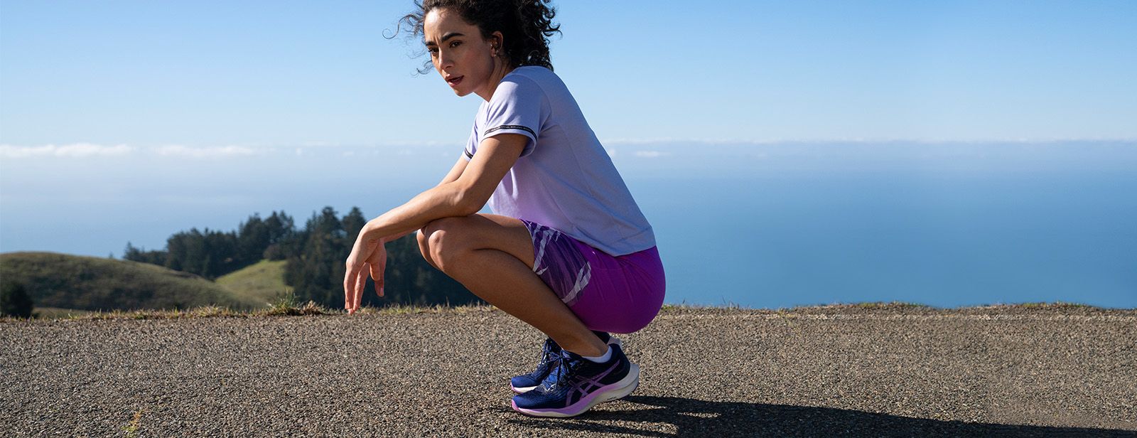Woman resting after run on top of mountain top in ASICS clothing.