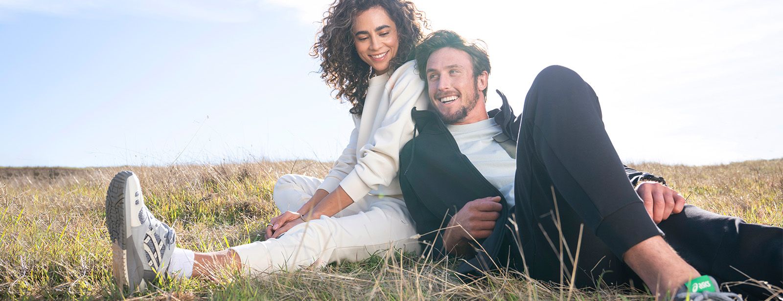 Man and woman in sustainable ASICS gear sitting in field.