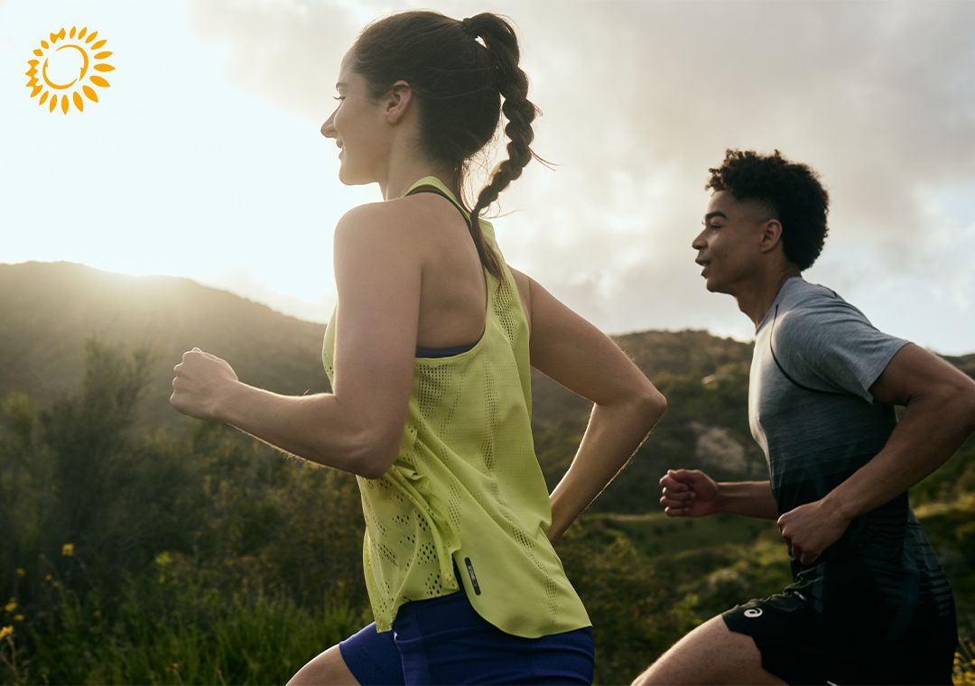 A male and female runner run through the hills at sunset.